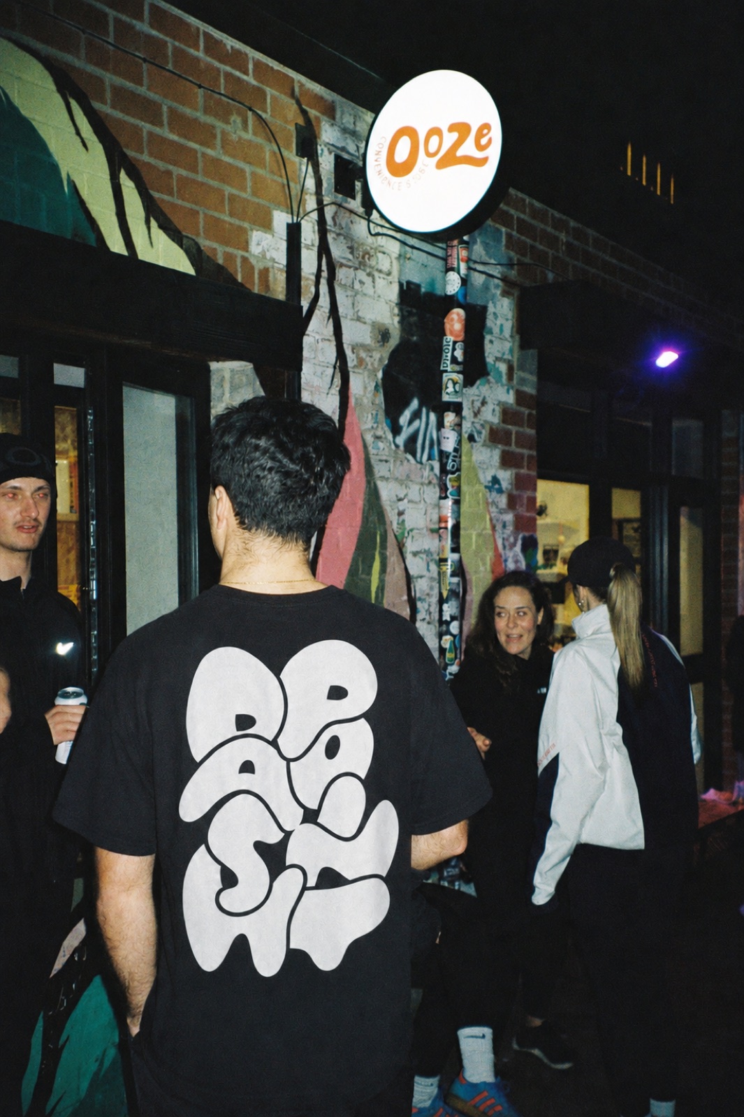 The DashPoint Tee in black, worn on a street at night, with the bubble-lettered print across the back