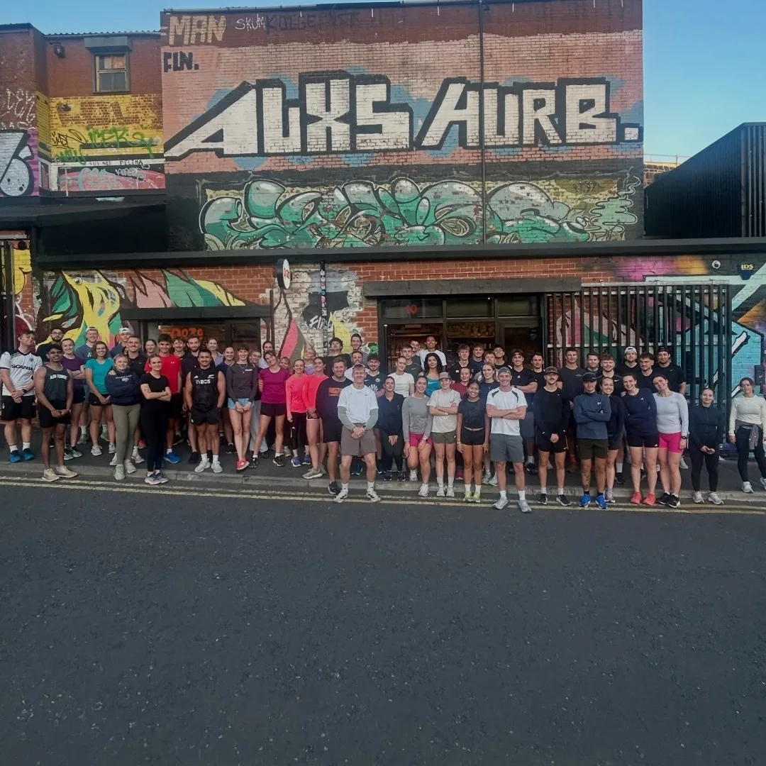 Collective Run Club lined up along a street beneath a wall of graffiti murals