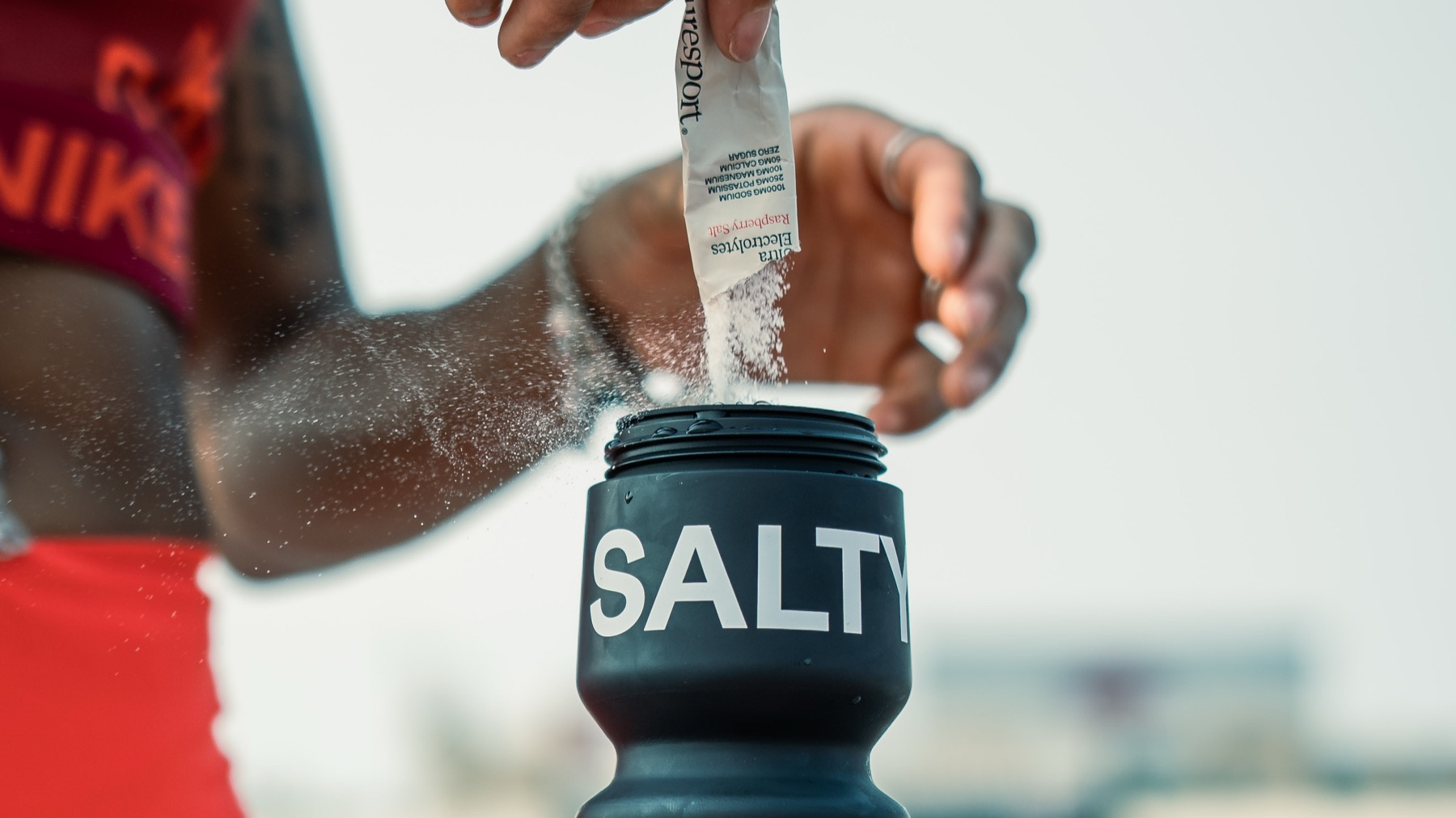 A runner pouring a sachet of Puresport Ultra Electrolytes into a black SALTY water bottle